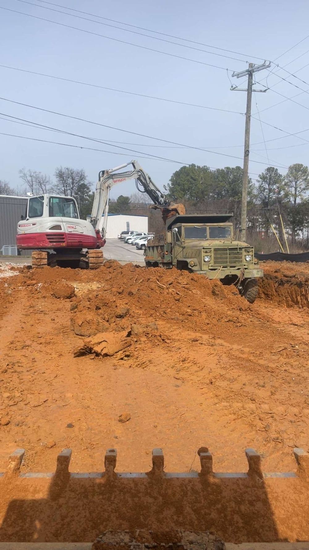 Military humvee and excavator at a construction site with muddy terrain.