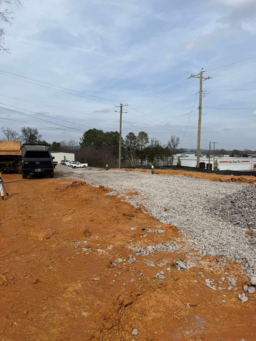 Construction site with gravel, orange earth, power lines, and vehicles in the background.