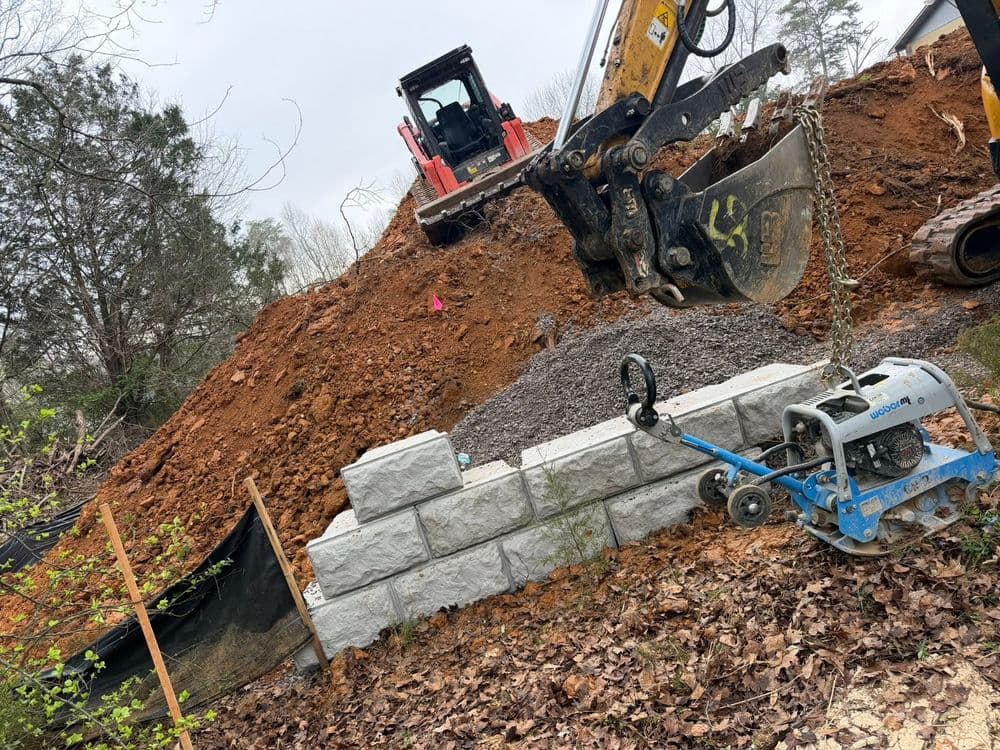 Excavation site with heavy machinery, gravel, and stone wall foundation under construction.
