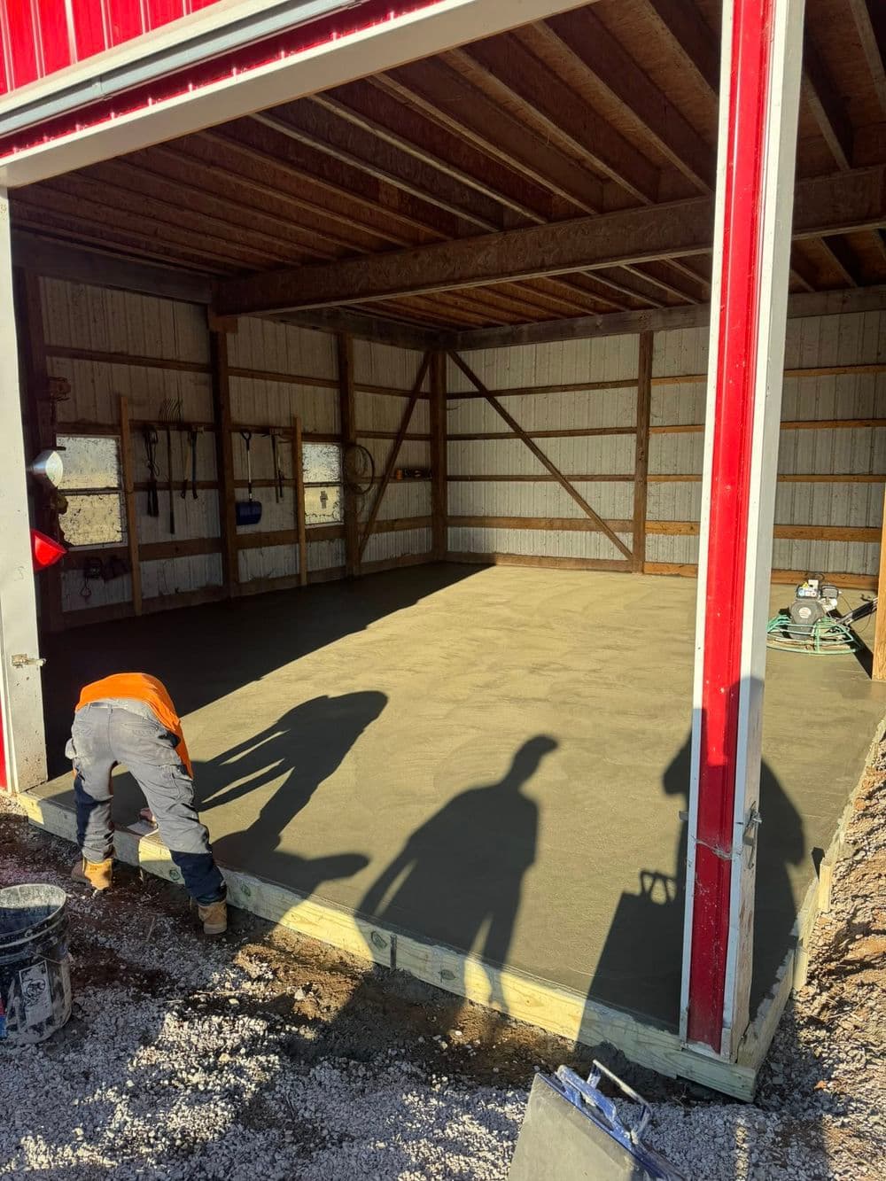 Construction workers pouring concrete in a newly built shed with red barn doors.