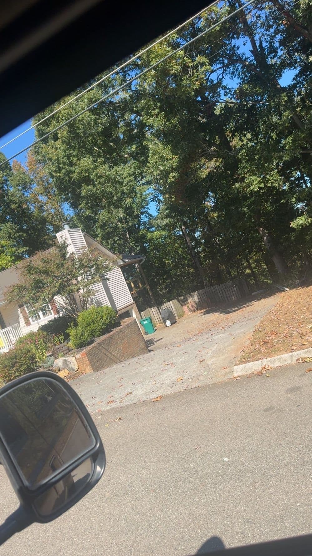 View of a residential driveway with a house surrounded by trees on a sunny day.
