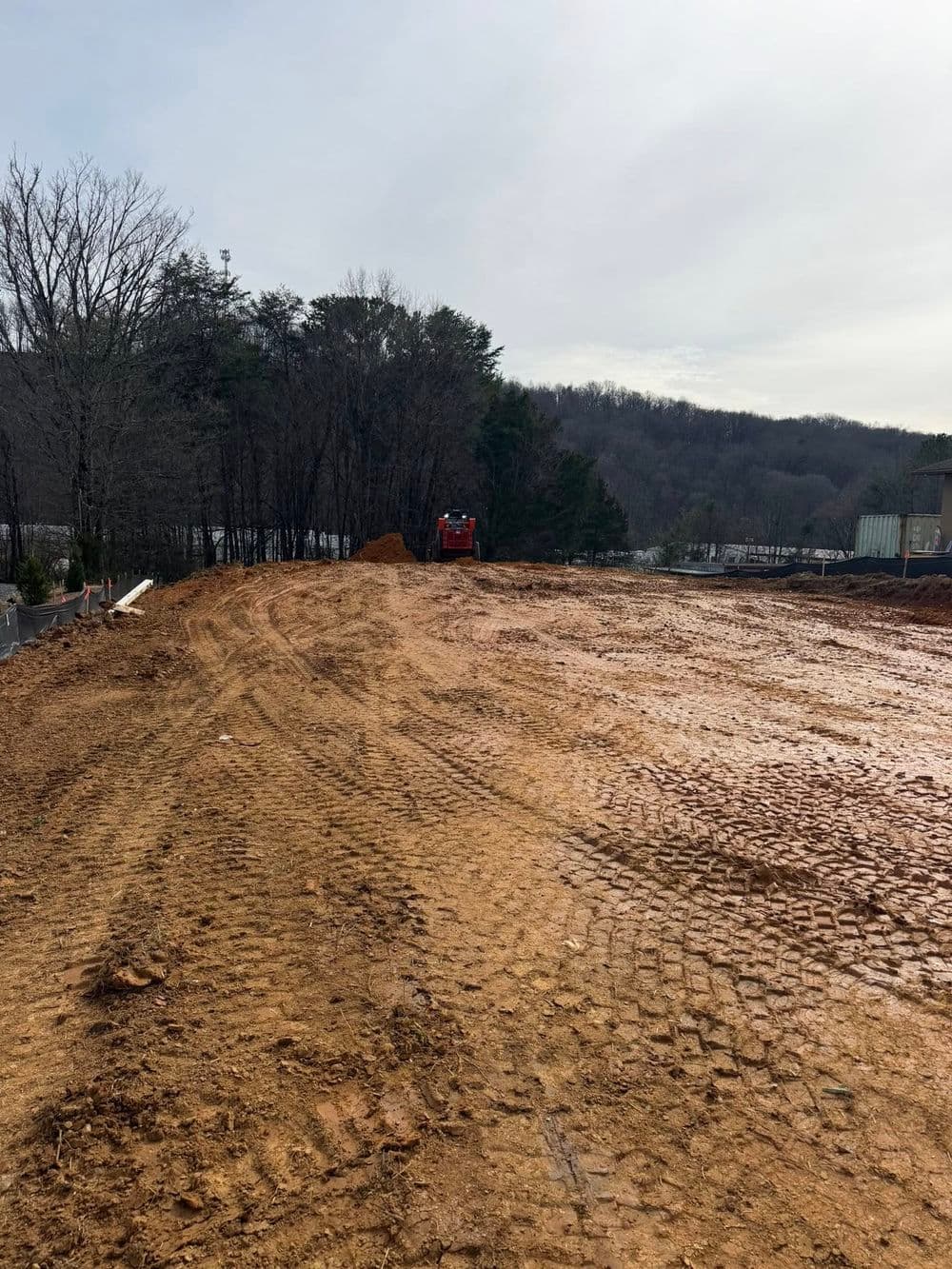 Construction site with freshly graded earth, heavy machinery in background, trees lining the area.