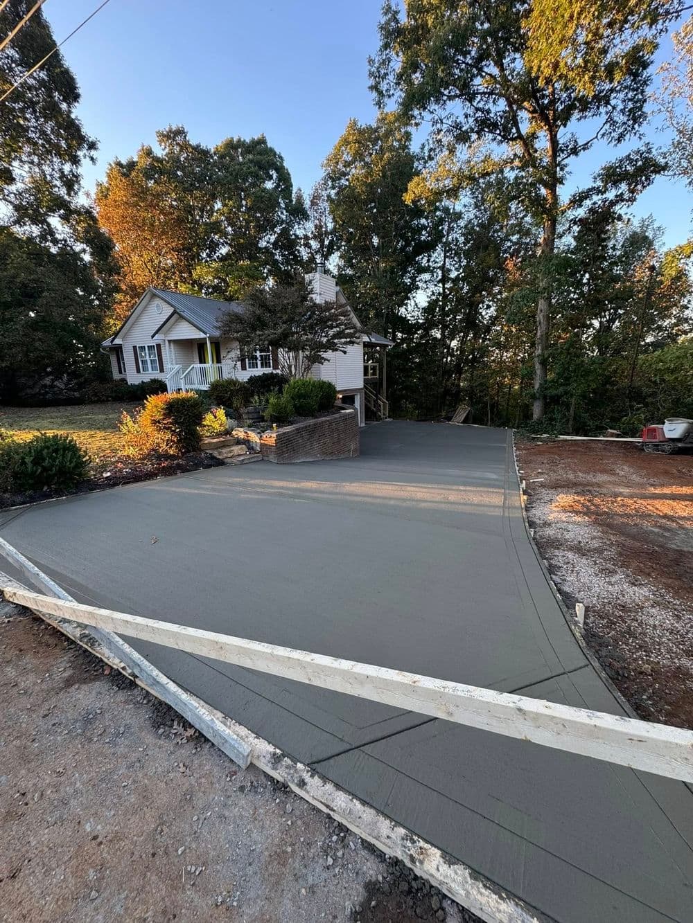 Newly poured concrete driveway in front of a house surrounded by trees.