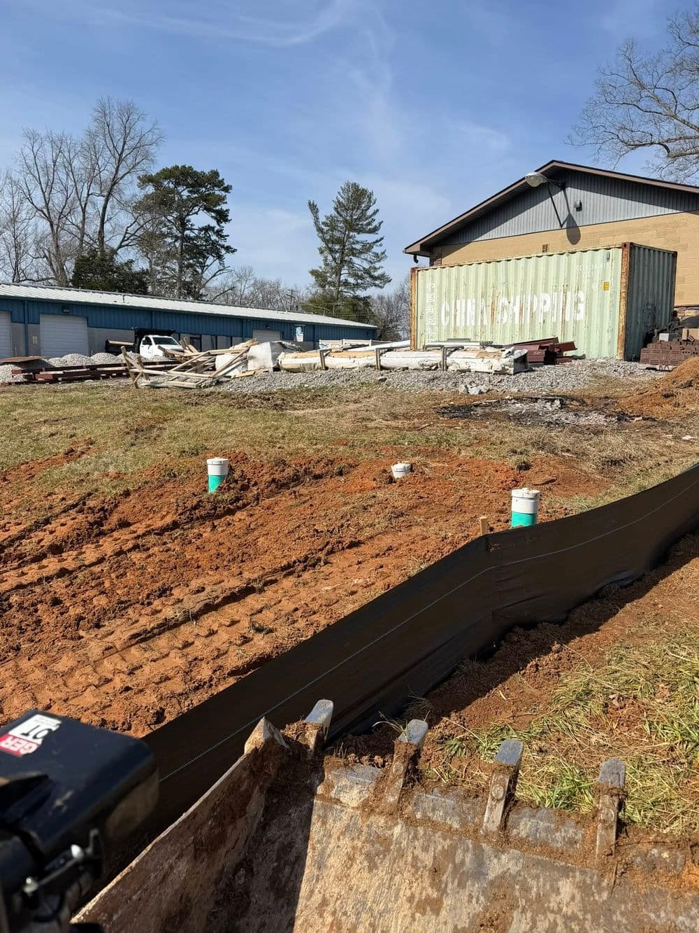 Construction site with ground preparation, debris at the building, and shipping container visible.