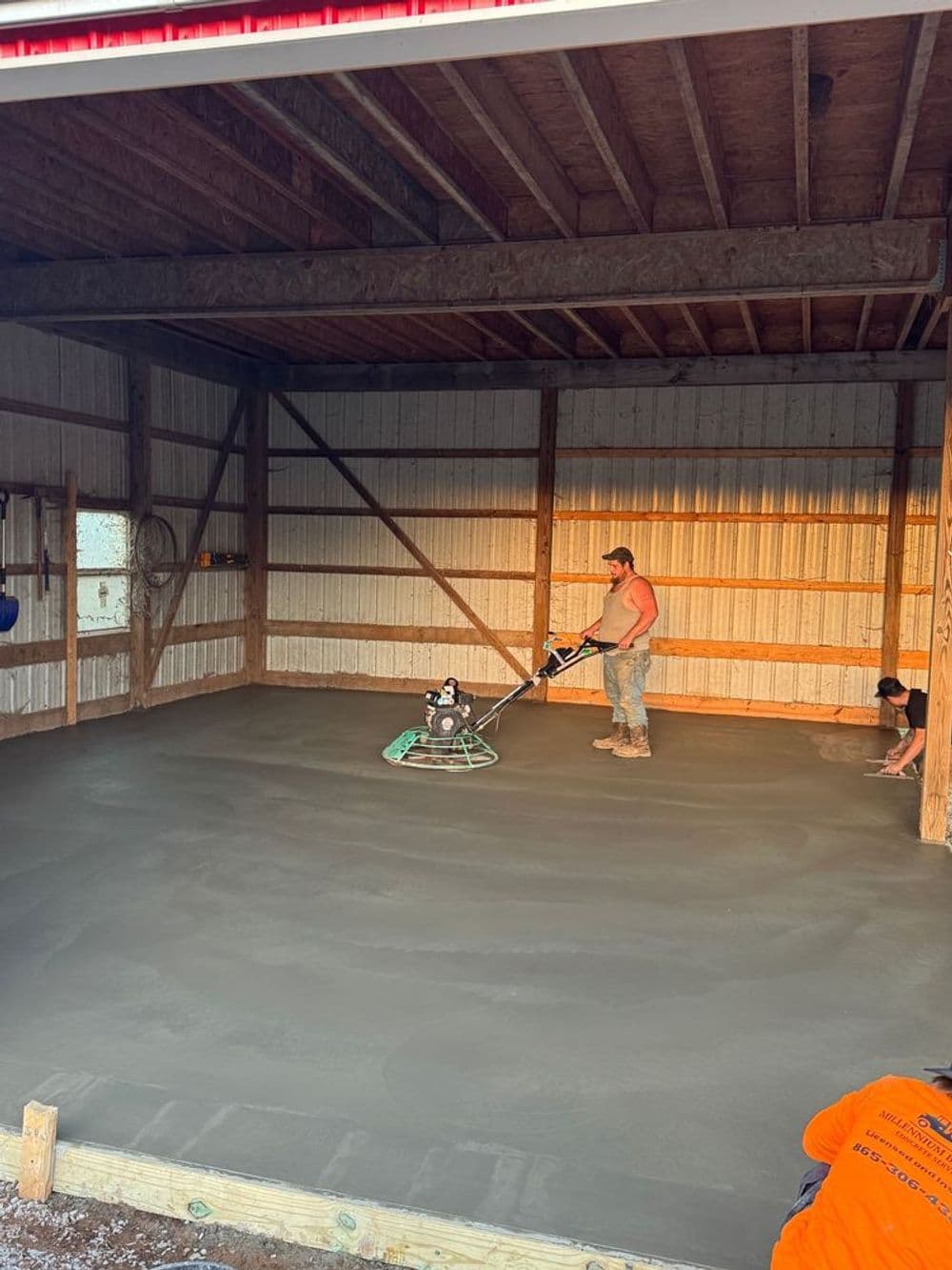 Workers finishing a concrete floor in a newly built shed during sunset.