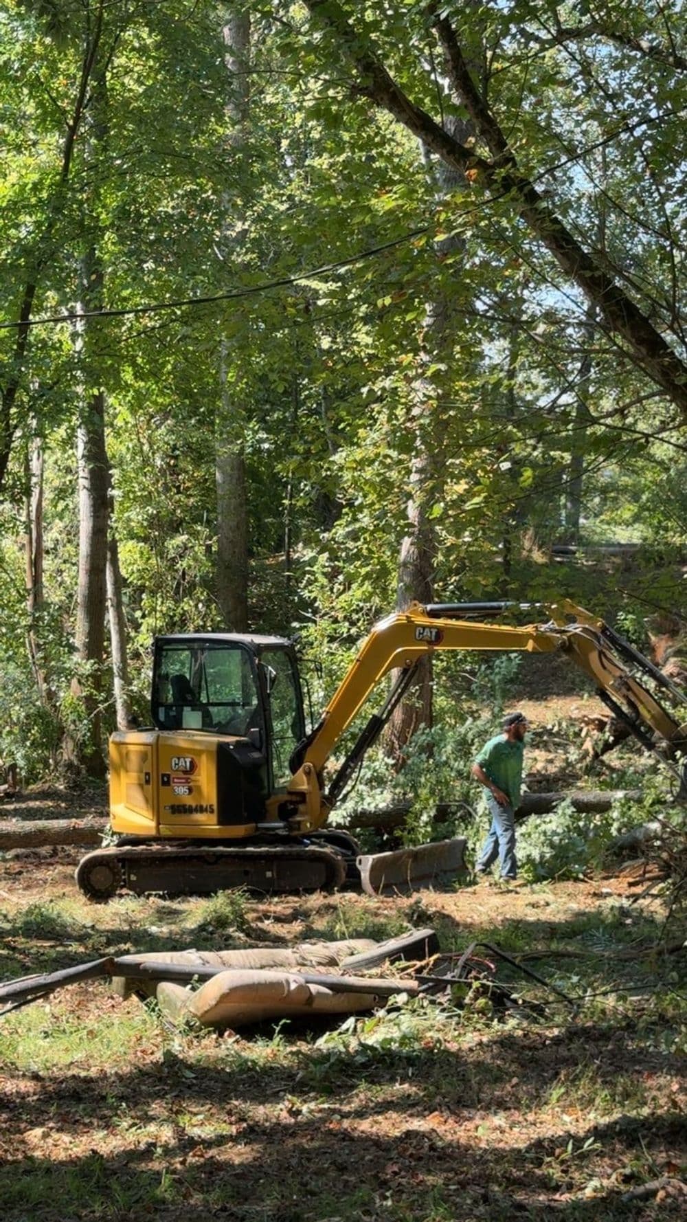 Excavator working in forested area, with operator clearing debris and foliage.