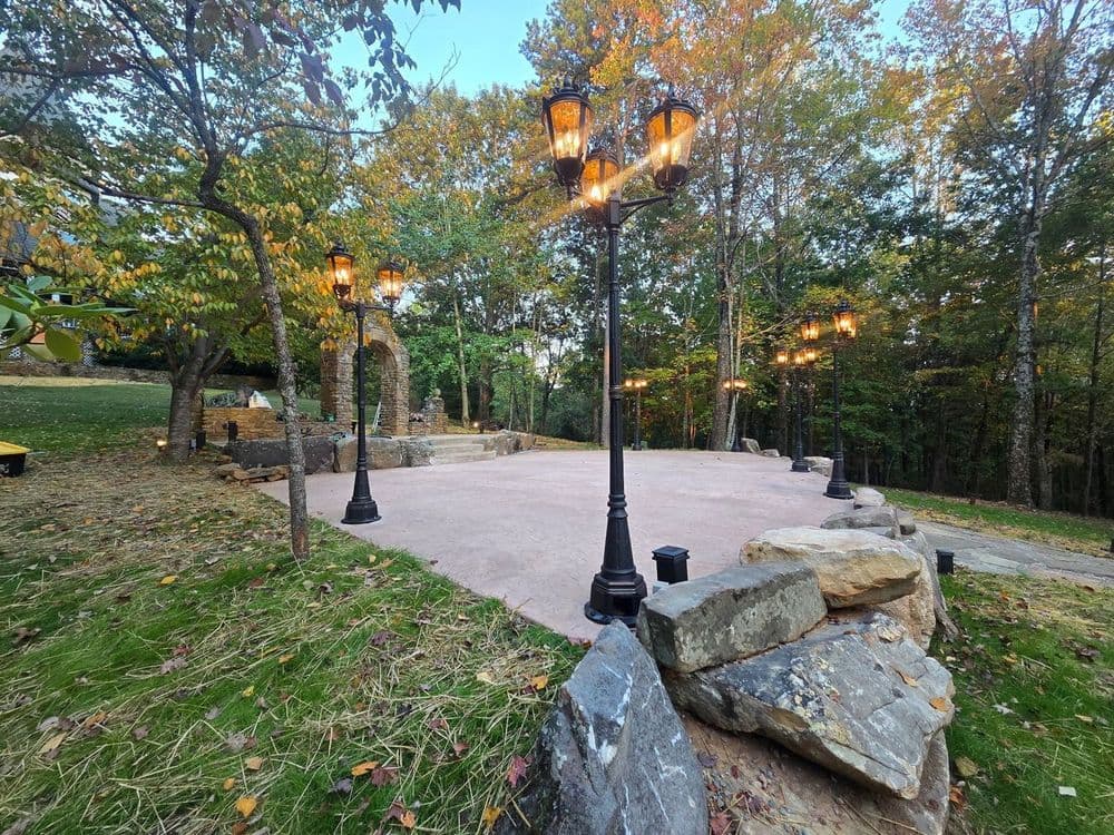 Outdoor gathering space with stone features and lighted lamp posts surrounded by autumn trees.